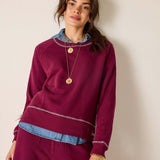 Woman wearing a burgundy sweater with denim collar against a beige background
