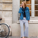 Woman in denim jacket and striped pants standing next to a bicycle against a building.