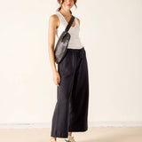 Woman wearing a white tank top, black wide-leg pants, and a black crossbody bag on a plain background