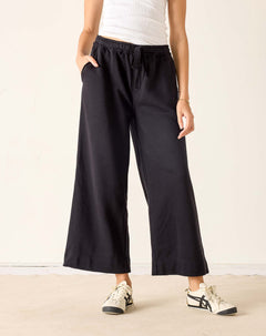 Person wearing black wide-leg pants and white sneakers on a plain background