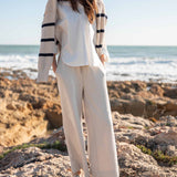 Bone wide-leg pants paired with a white knit top and striped cardigan on a beach.