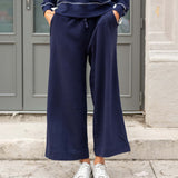 Person wearing a navy tracksuit with white sneakers standing in front of a gray door.