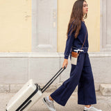 Woman in navy outfit pulling a white suitcase on a street.