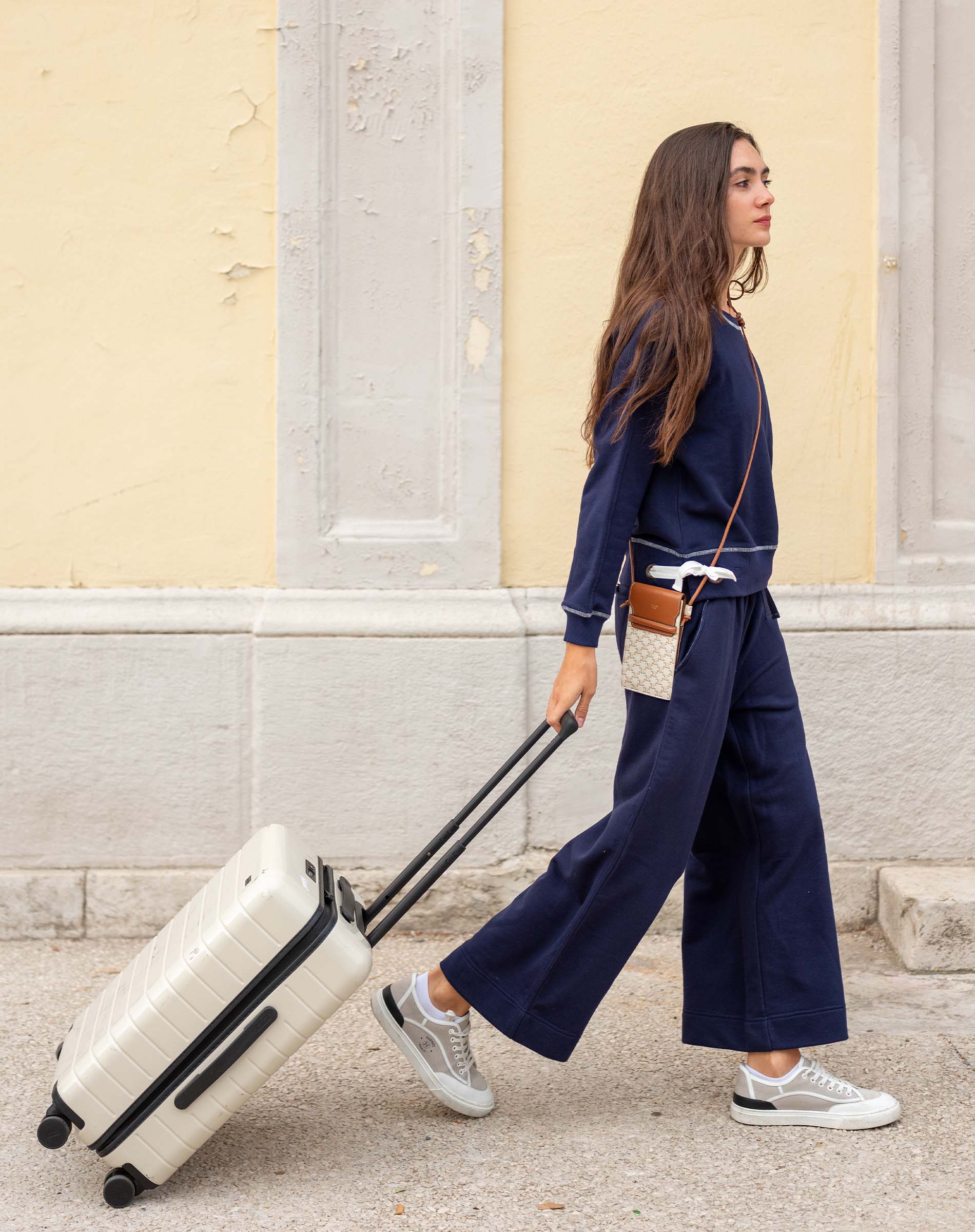 Woman in navy outfit pulling a white suitcase on a street.