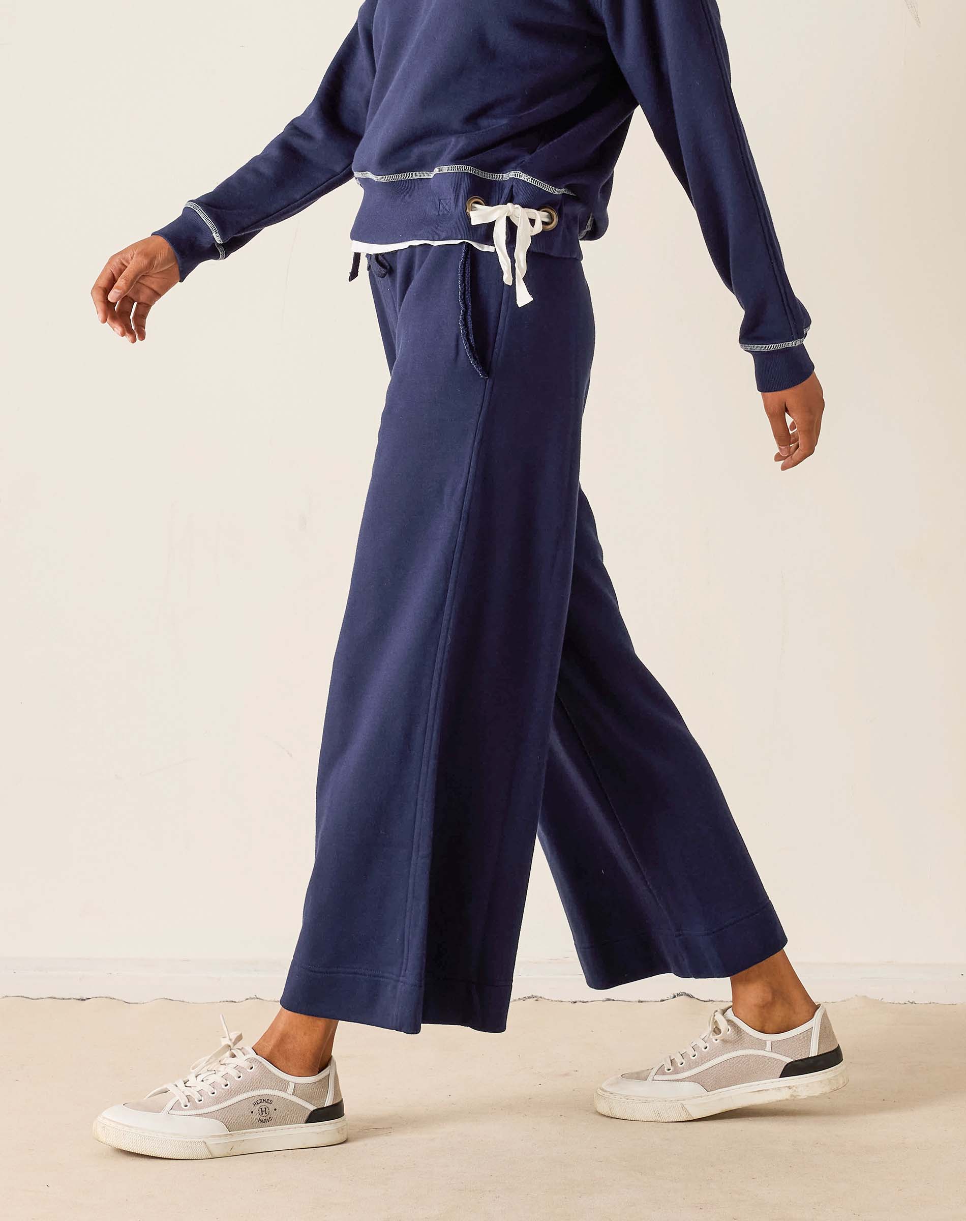 Person wearing navy blue sweatpants and a matching top on a beige background