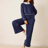Woman wearing a navy tracksuit with white sneakers on a plain background