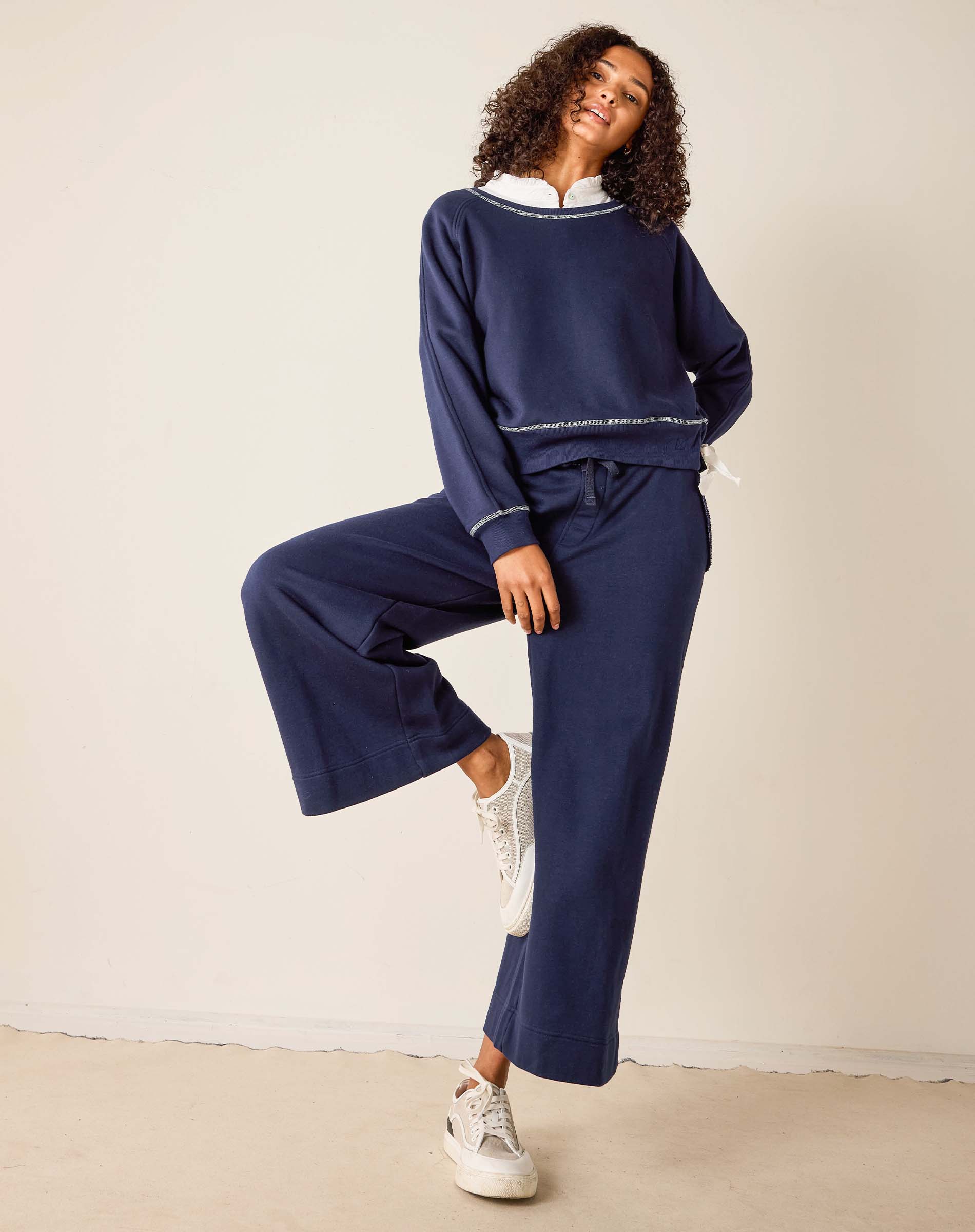 Woman wearing a navy tracksuit with white sneakers on a plain background