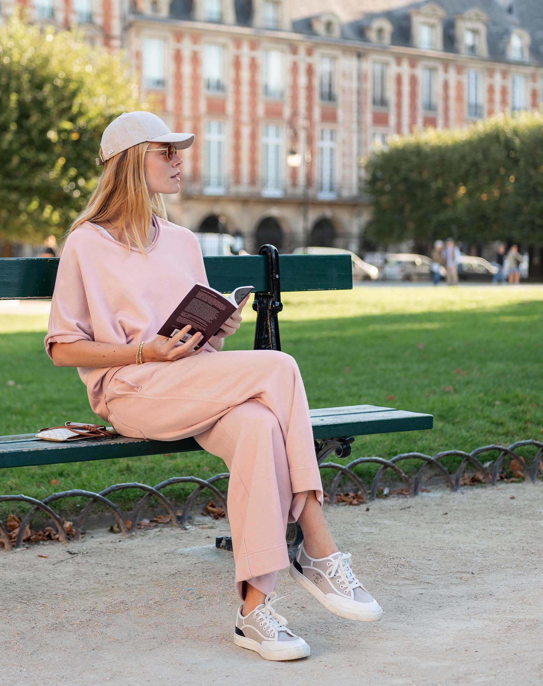 Woman in a pink outfit sitting on a bench in an urban park.