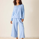 Woman wearing a light blue outfit with wide-leg pants against a plain background