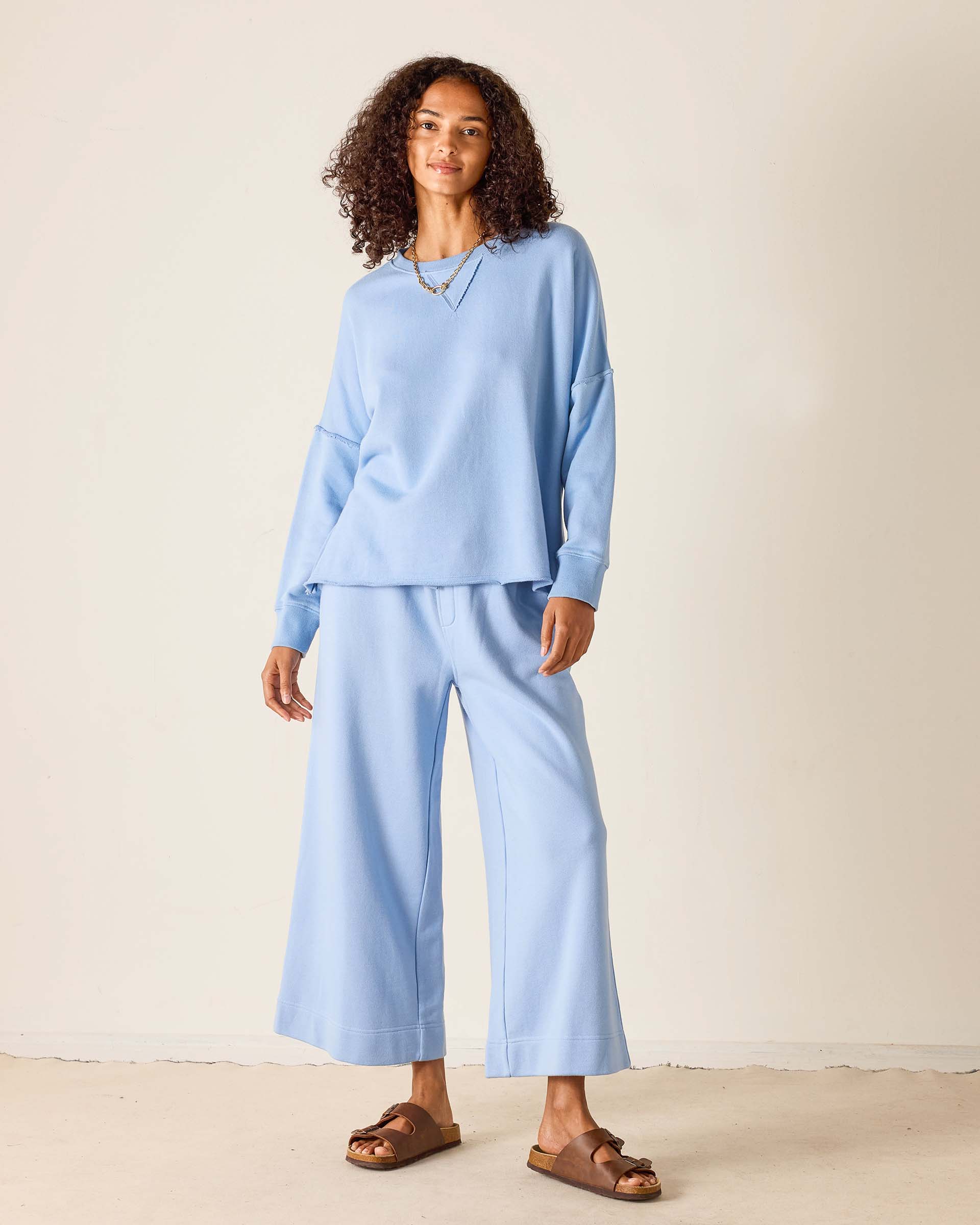 Woman wearing a light blue outfit with wide-leg pants against a plain background