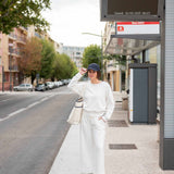 Person standing at a bus stop wearing a white outfit with a black cap.
