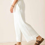 Person wearing white pants and brown sandals on a plain background