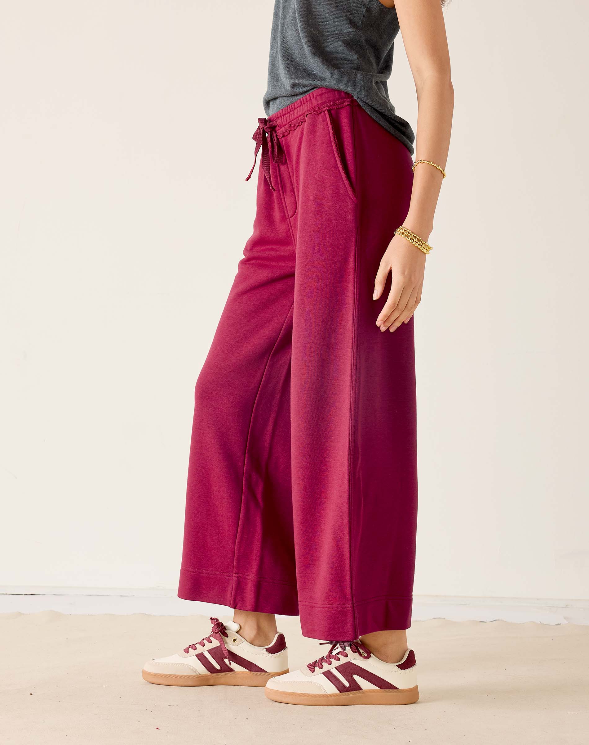 Person wearing maroon wide-leg pants with a gray top and white sneakers on a light background