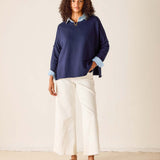 Woman wearing a navy sweater and white pants against a beige background