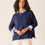 Woman wearing a navy blue sweater over a light blue shirt with white pants on a beige background