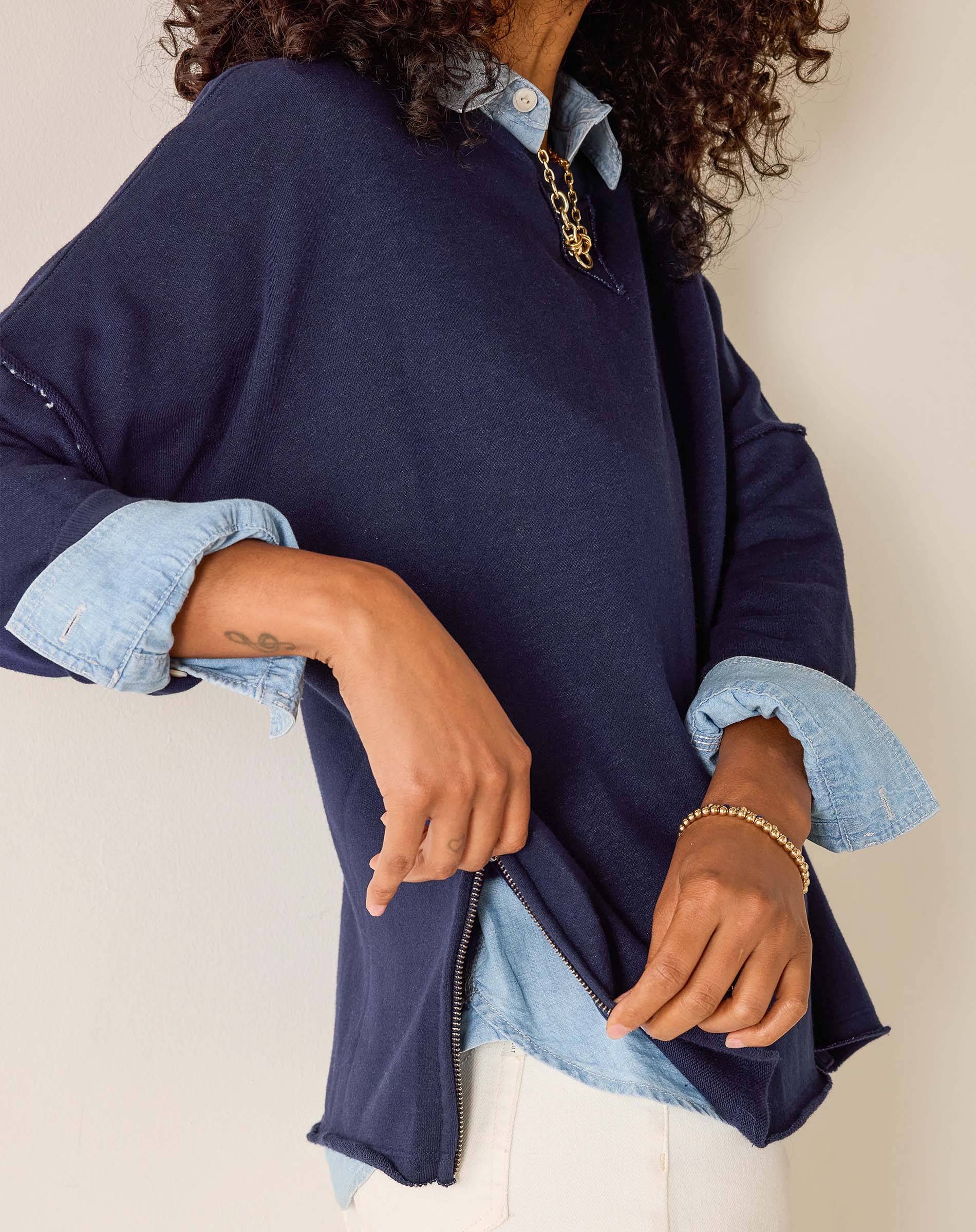 Person wearing a navy blue jacket with denim sleeves and cuffs, on a plain background.