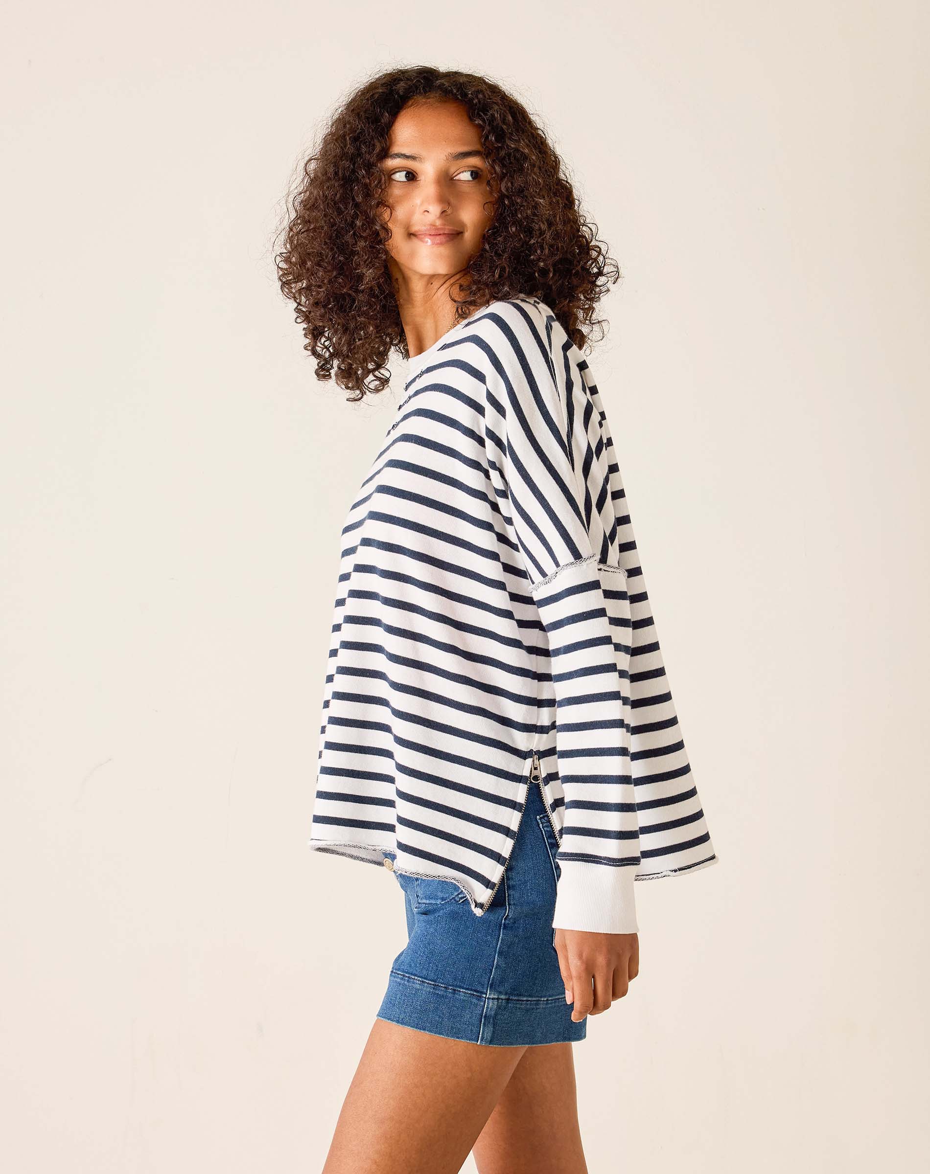 Woman wearing a striped sweater and denim shorts on a plain background