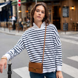 Woman in a striped sweater with a brown bag standing on a city street.