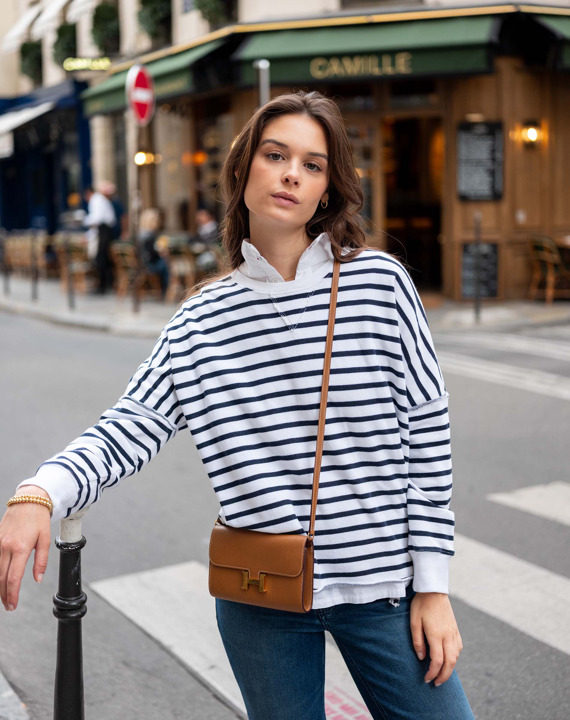 Woman in a striped sweater with a brown bag standing on a city street.