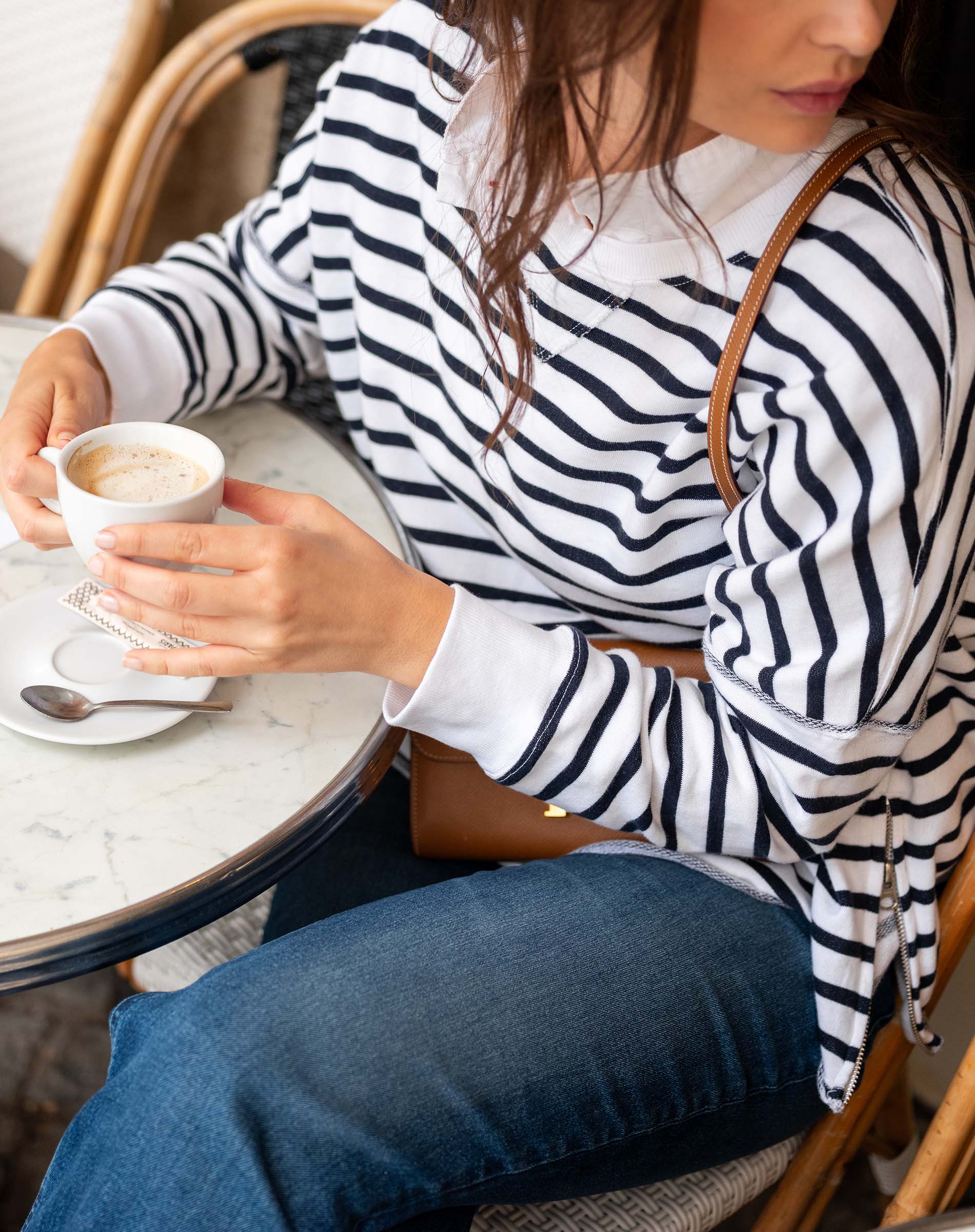 Woman in a striped sweater holding a cup of coffee at a cafe.
