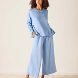 Woman wearing a light blue outfit with wide-leg pants against a plain background