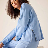 Woman wearing a light blue tracksuit sitting on a white stool against a beige background