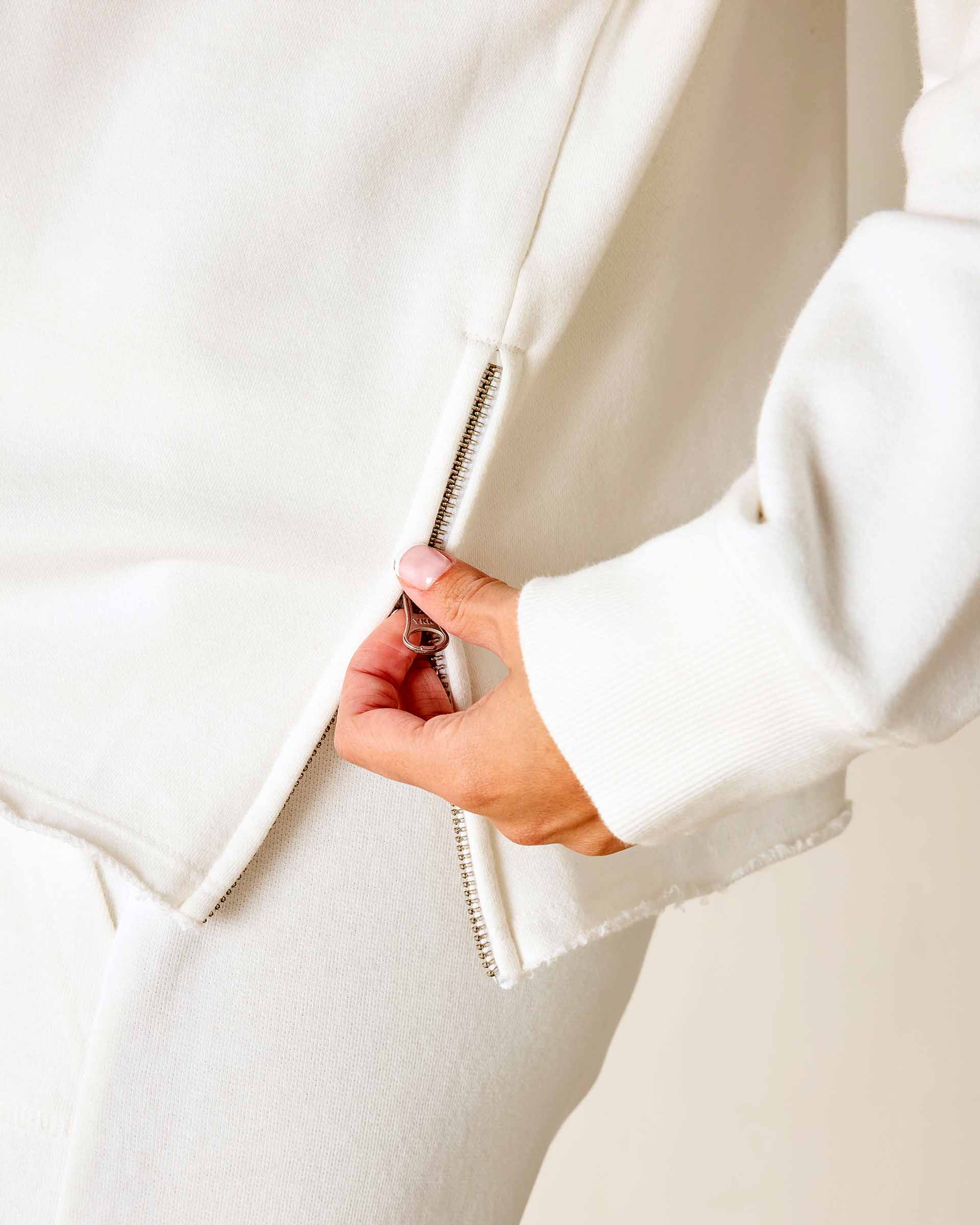 Close-up of a hand zipping up a white hoodie