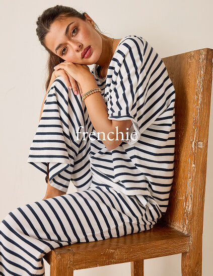 Woman wearing a black and white striped outfit sitting on a wooden chair with 'frenchie' branding.