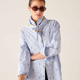 Woman wearing a blue and white striped shirt with a pattern, standing against a plain background.
