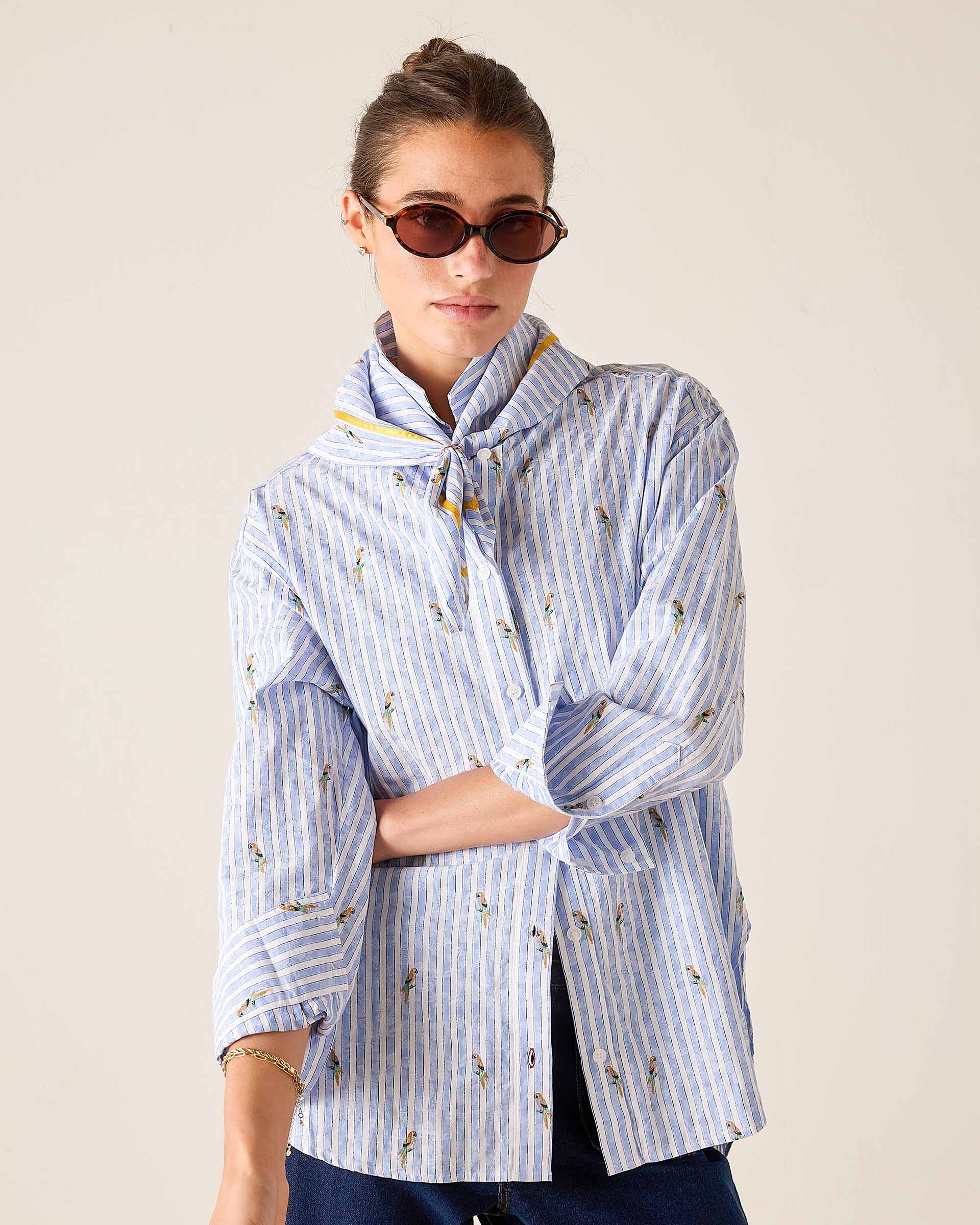 Woman wearing a blue and white striped shirt with a pattern, standing against a plain background.