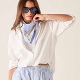 Woman wearing a white blouse, blue striped scarf, and light blue pants with a white background