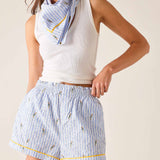 Woman wearing a white sleeveless top and blue striped shorts with a matching scarf.