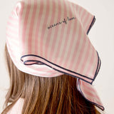 Pink striped headscarf with 'acorns of love' text worn by a person on a plain background