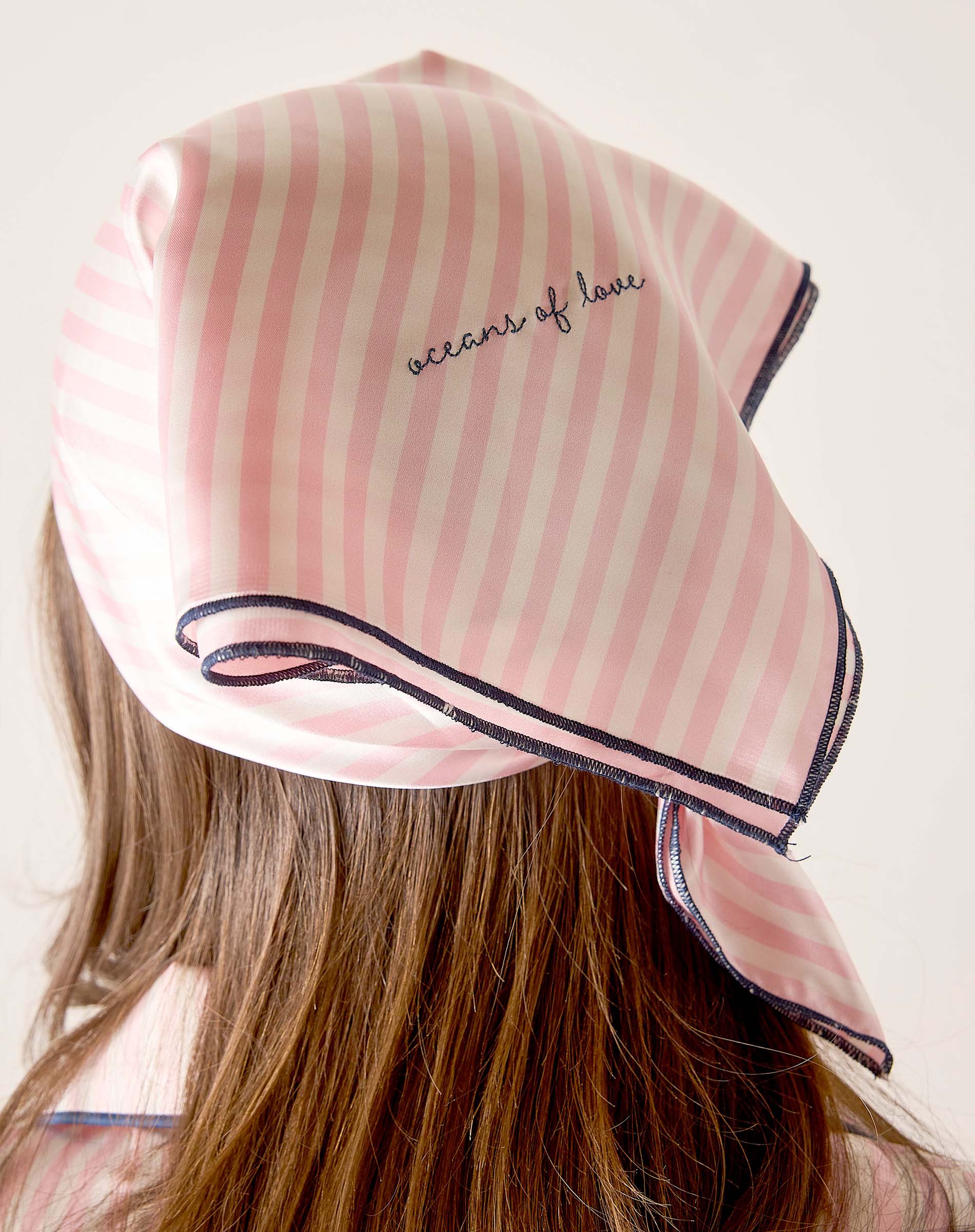 Pink striped headscarf with 'acorns of love' text worn by a person on a plain background