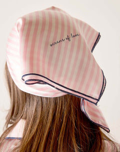 Pink striped headscarf with 'acorns of love' text worn by a person on a plain background