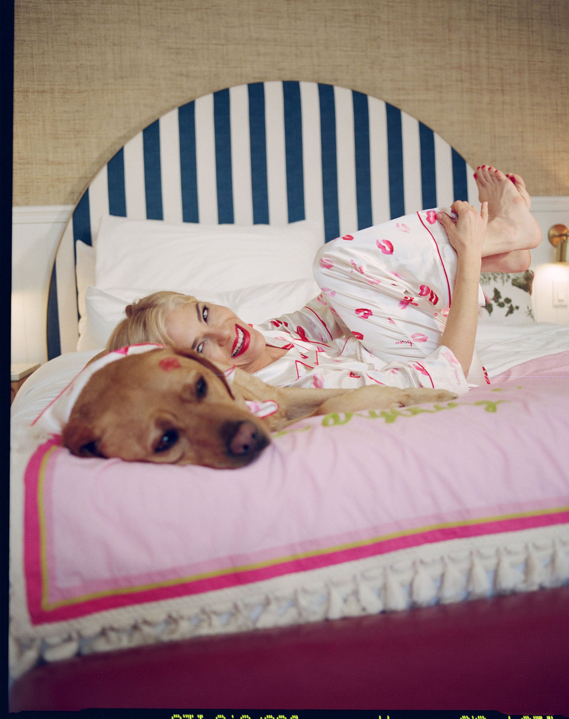 Woman in pajamas lying on a bed with a dog, wearing red lipstick.