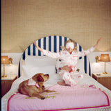 Woman in pajamas sitting on a bed with a dog, wearing a face mask, in a room with striped headboard and lamps.