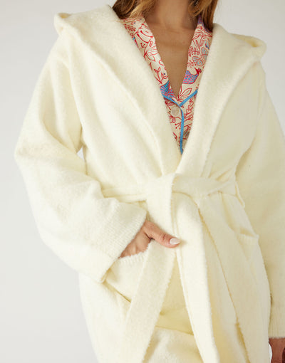 detail shot of women wearing cream, fuzzy hooded robe over print pajama set tied with hand in front pocket