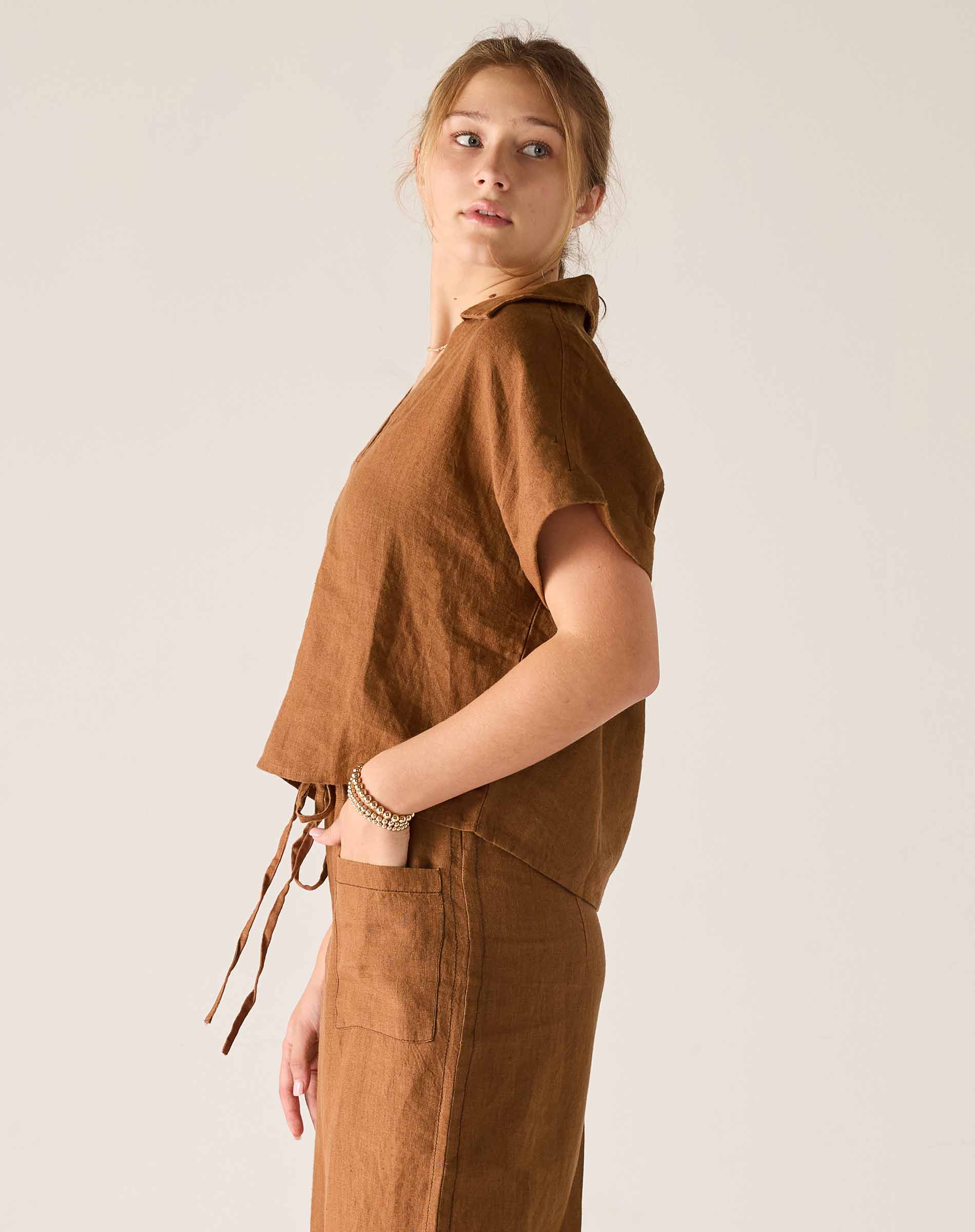 Woman wearing a brown sleeveless top and pants against a plain background