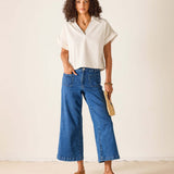 Woman wearing a white blouse and blue jeans against a plain background