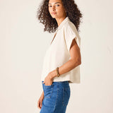 Woman wearing a beige sleeveless top and blue jeans against a plain background