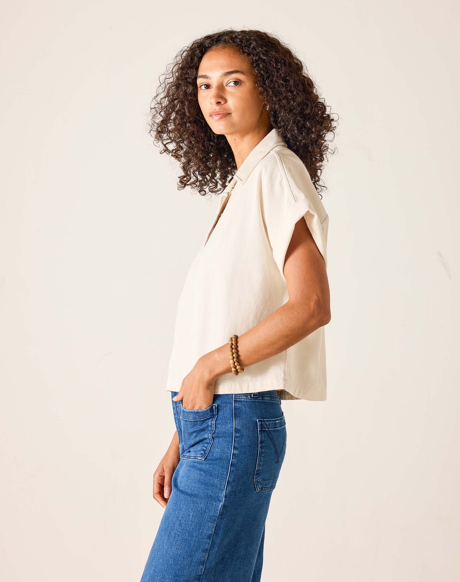 Woman wearing a beige sleeveless top and blue jeans against a plain background