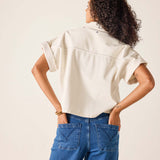 Person wearing a beige shirt and blue jeans against a plain background