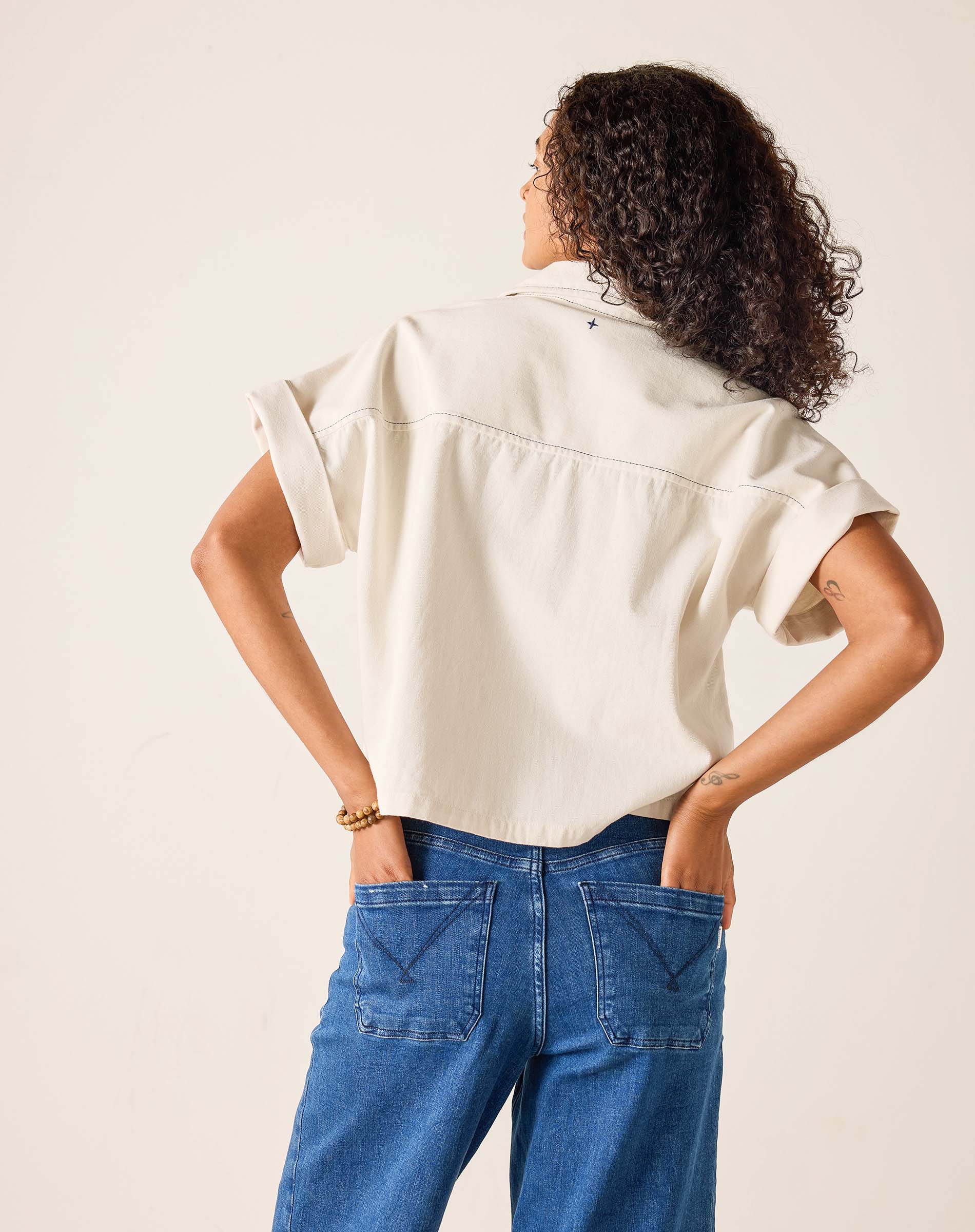 Person wearing a beige shirt and blue jeans against a plain background