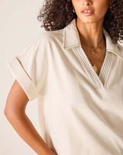 Woman wearing a beige short-sleeve shirt with a neutral background