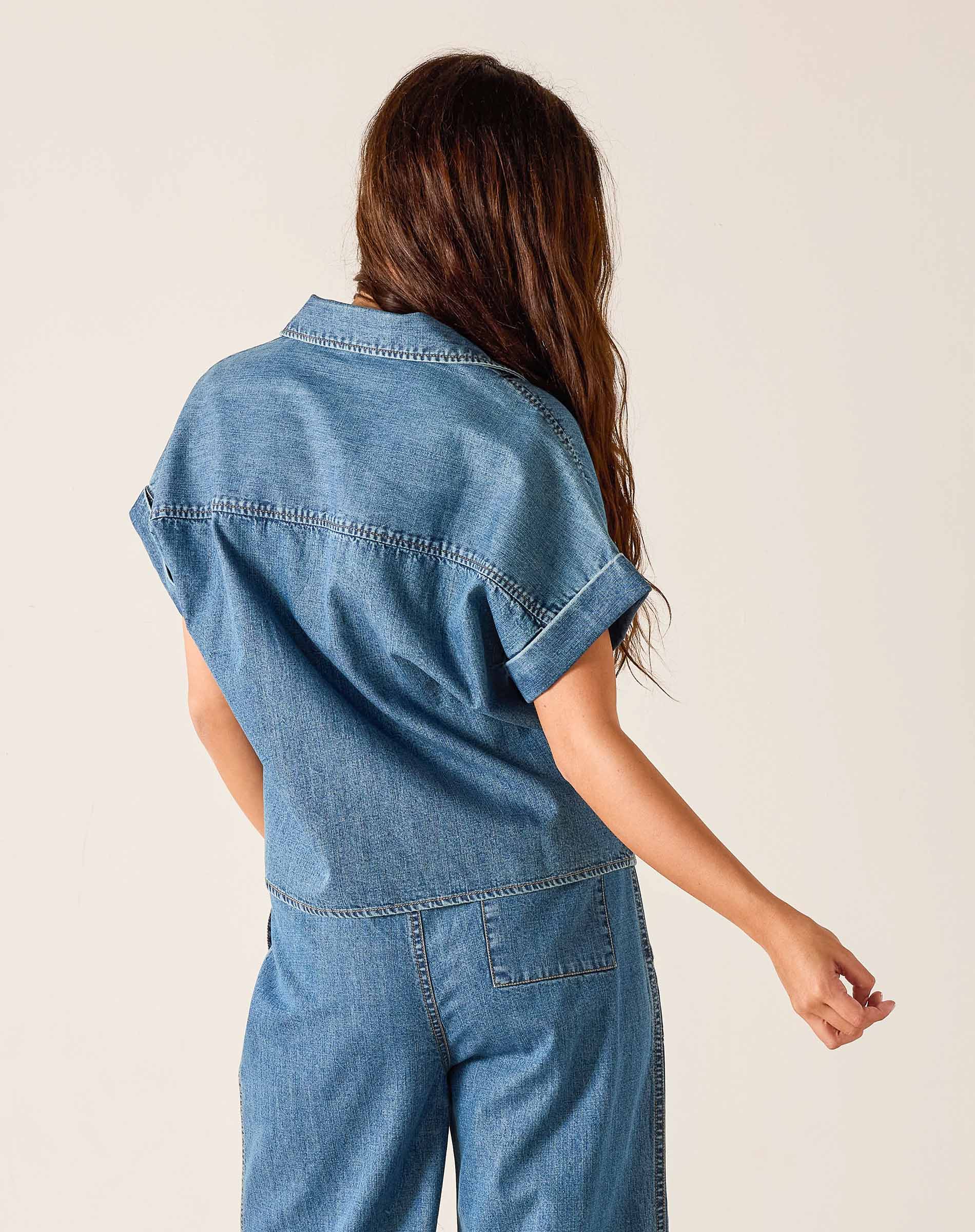 Person wearing a blue denim jumpsuit against a plain background