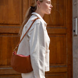 Woman holding a brown leather handbag in front of a wooden door