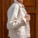 Person wearing a beige denim jacket in front of a wooden door