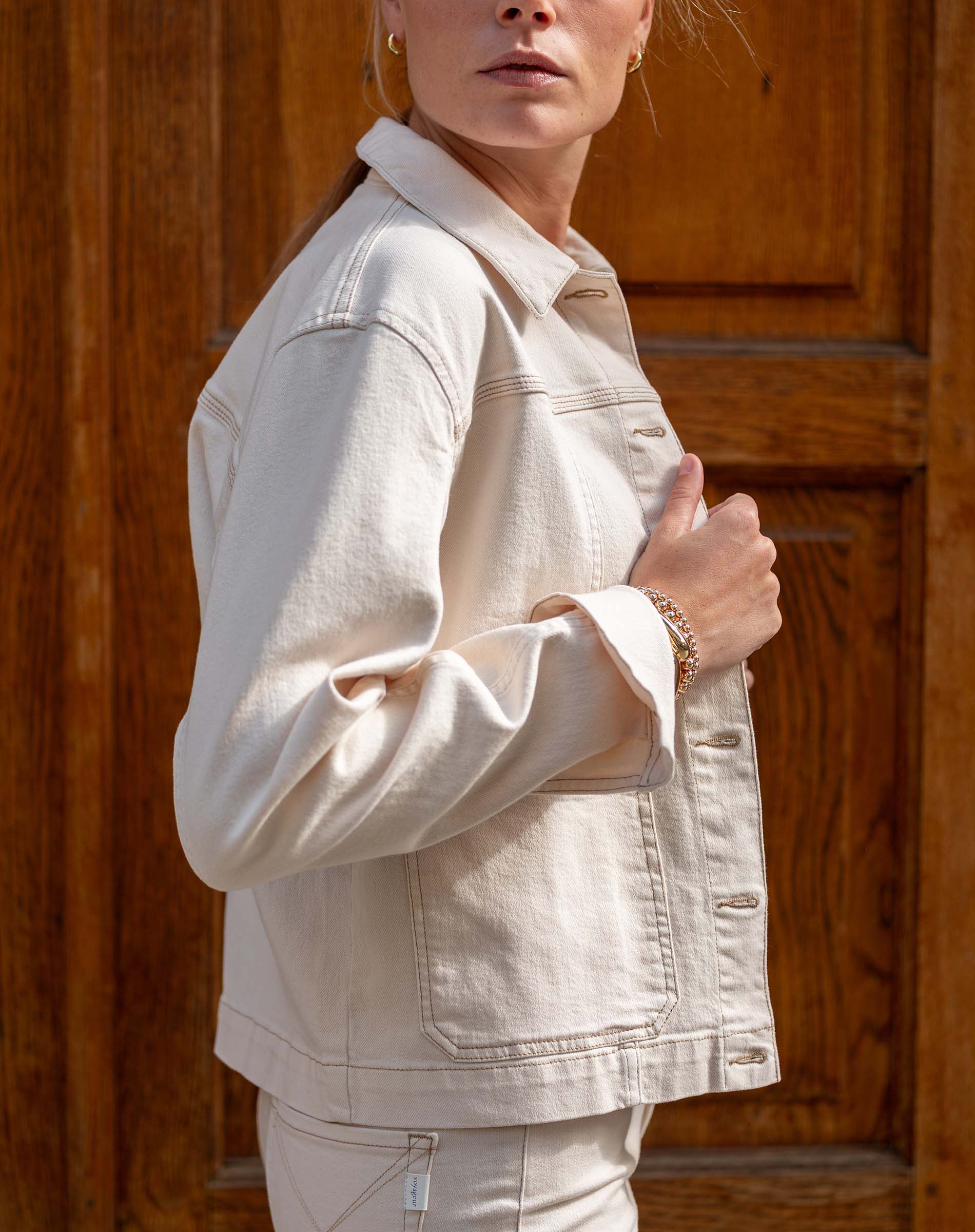 Person wearing a beige denim jacket in front of a wooden door