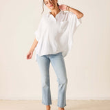Woman wearing a white shirt and light blue jeans against a plain background
